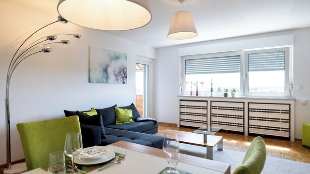 Een moderne woonkamer met een eethoek, een bank, een tafel gedekt voor twee personen en een raam met luxaflex.
