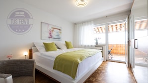 Een moderne slaapkamer met een bed, kussens, een nachtkastje, een stoel en een raam met uitzicht.