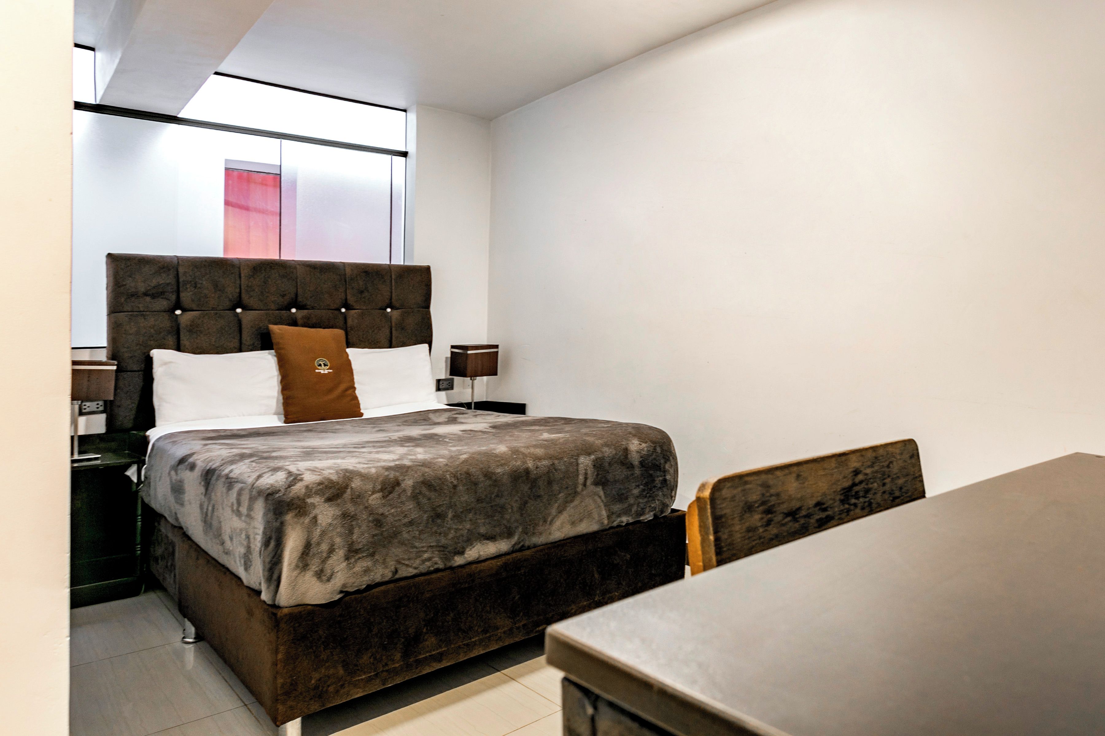 A bedroom with a bed, a nightstand, a bedside table, a chair, and a window.