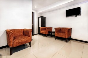 A hotel room with a flat-screen TV mounted on the wall, two patterned armchairs, a small table, and a cabinet. - Hidden Garden (Cusco)