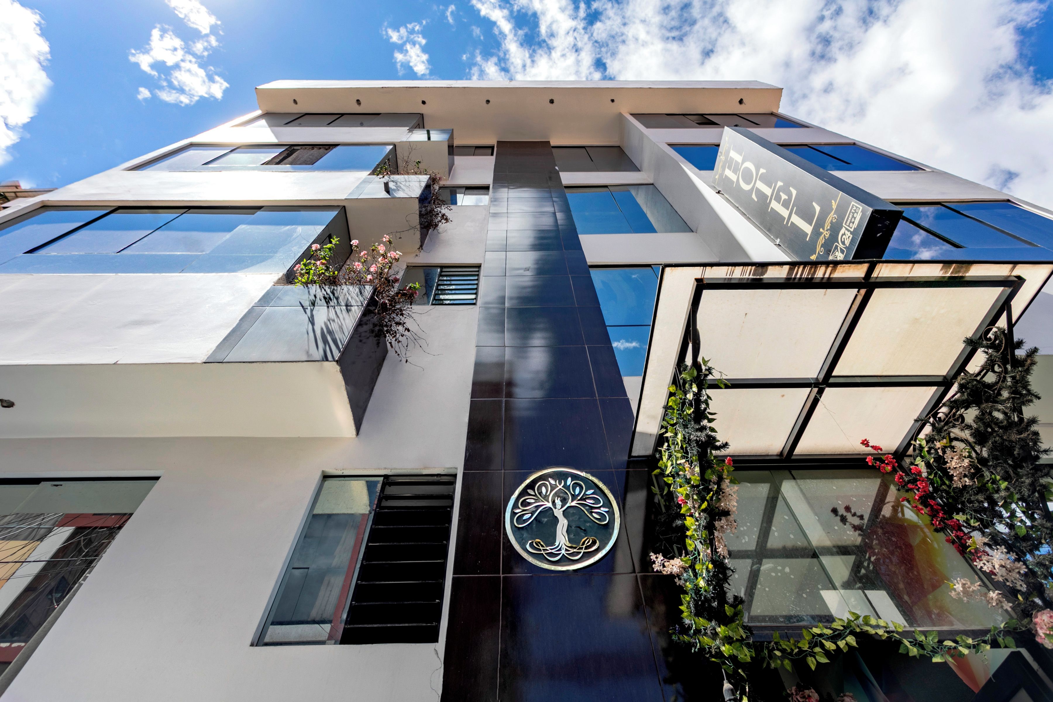 A modern building with a logo, large windows, and a balcony with plants.