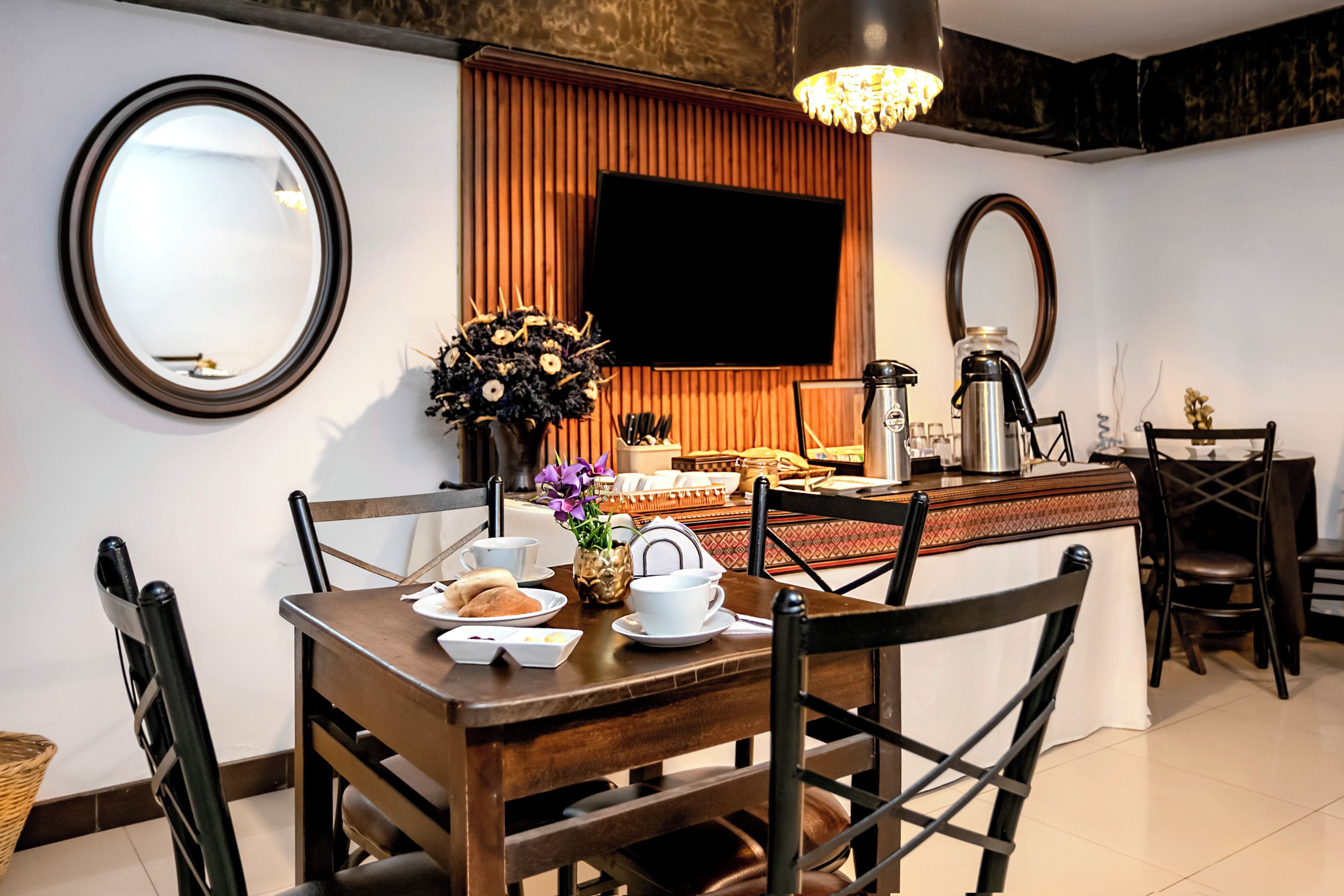 Un comedor con mesa de madera, sillas, un florero y un televisor de pantalla plana montado en la pared.