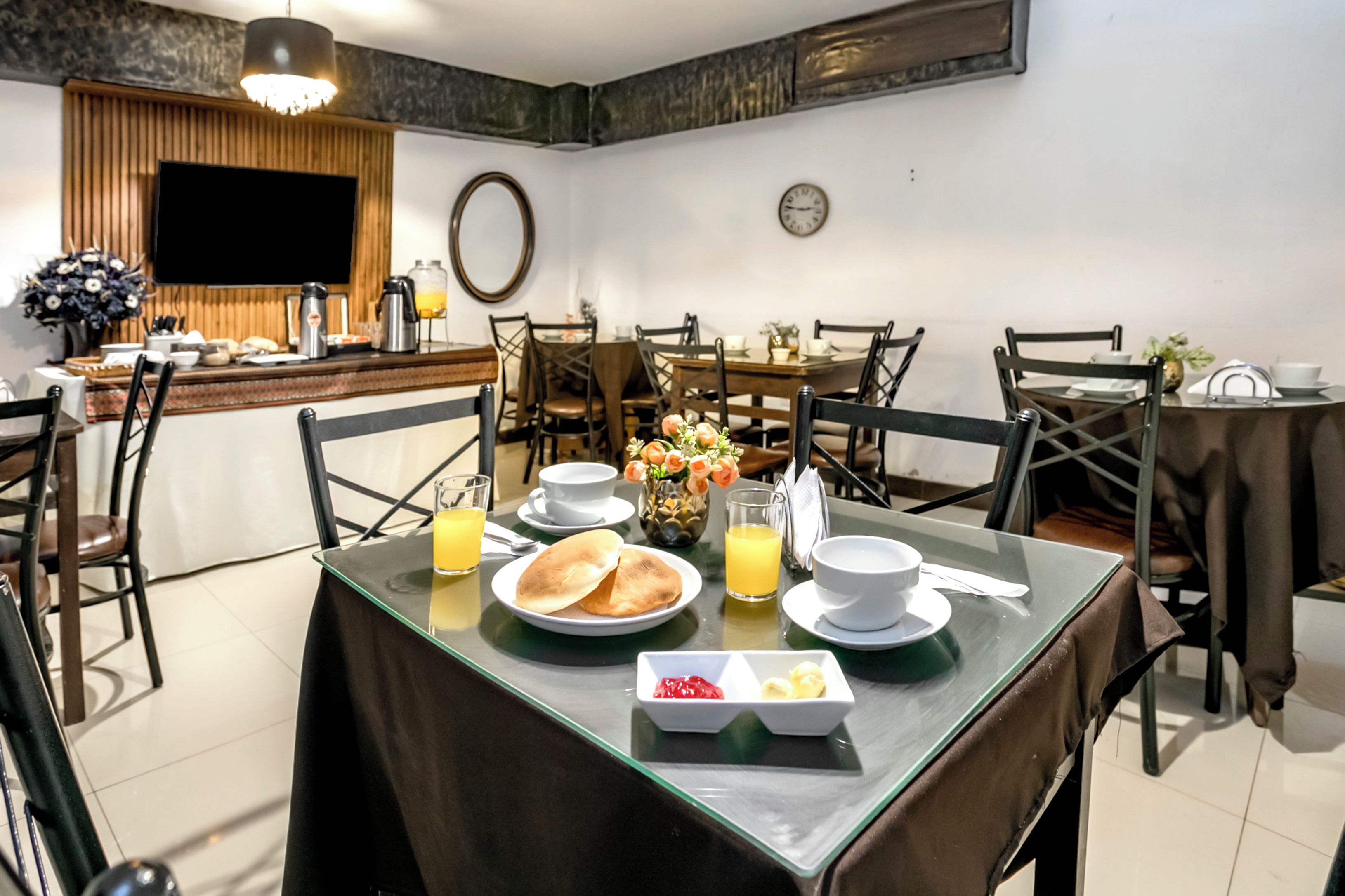 A breakfast setting with a table set for two, including plates, cups, and a fruit basket.