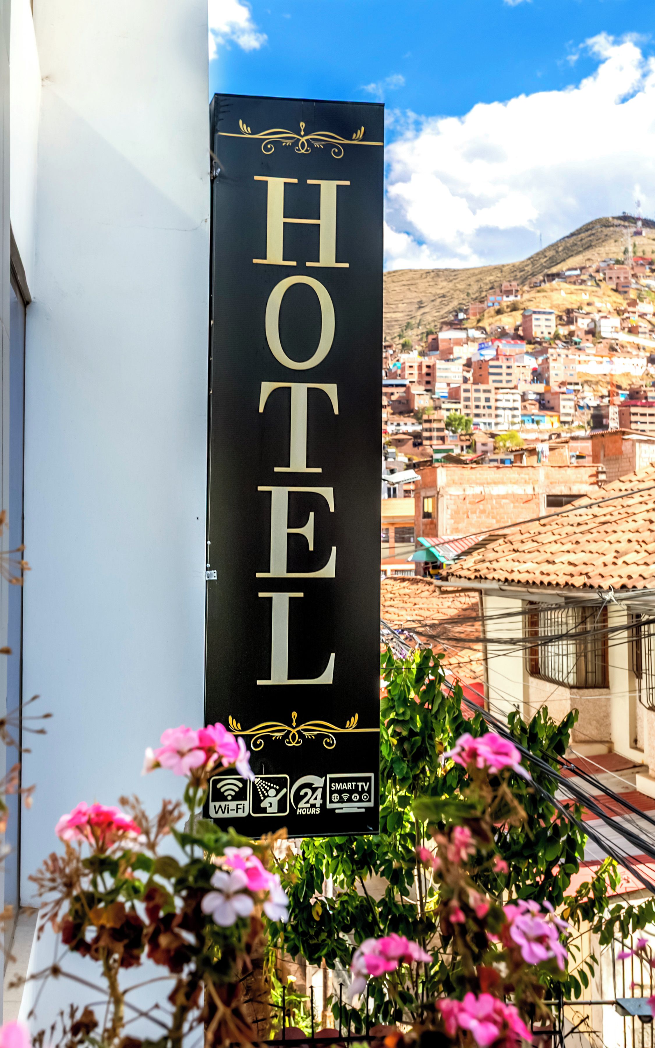 A hotel sign with 'HOTEL' written vertically, surrounded by flowers, with a view of a town in the background.