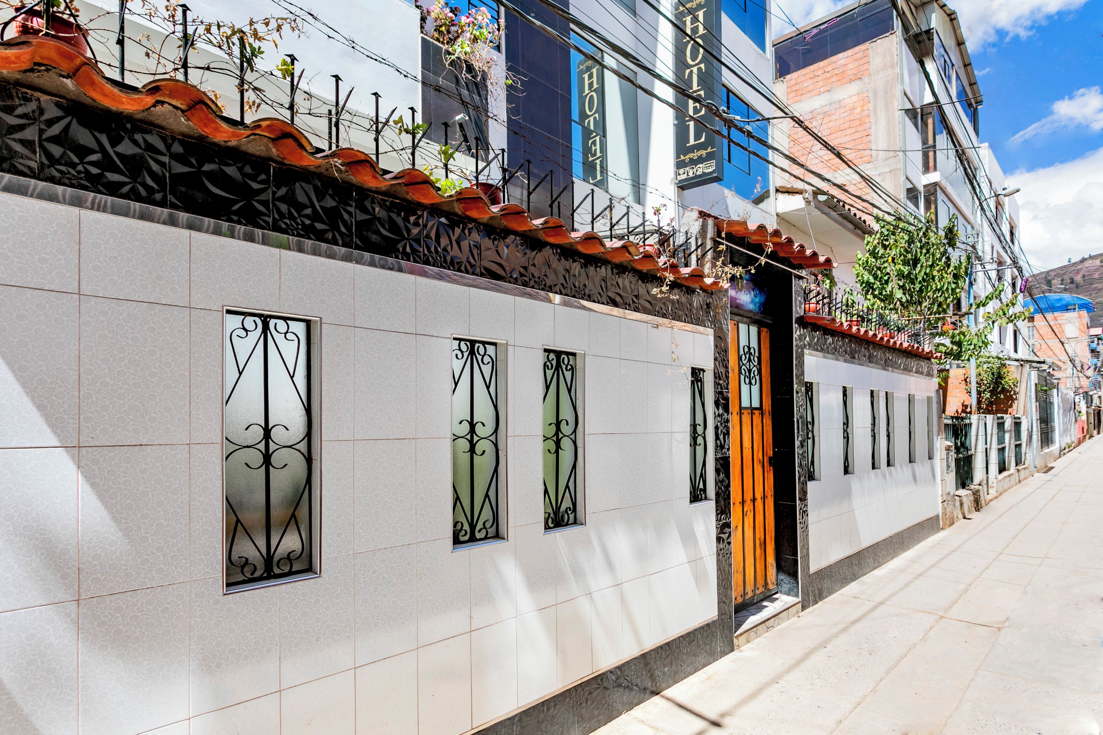 La façade d’un hôtel, recouverte de carreaux, présente de nombreuses fenêtres ornées de grilles en fer décoratives et un toit recouvert de tuiles rouges.