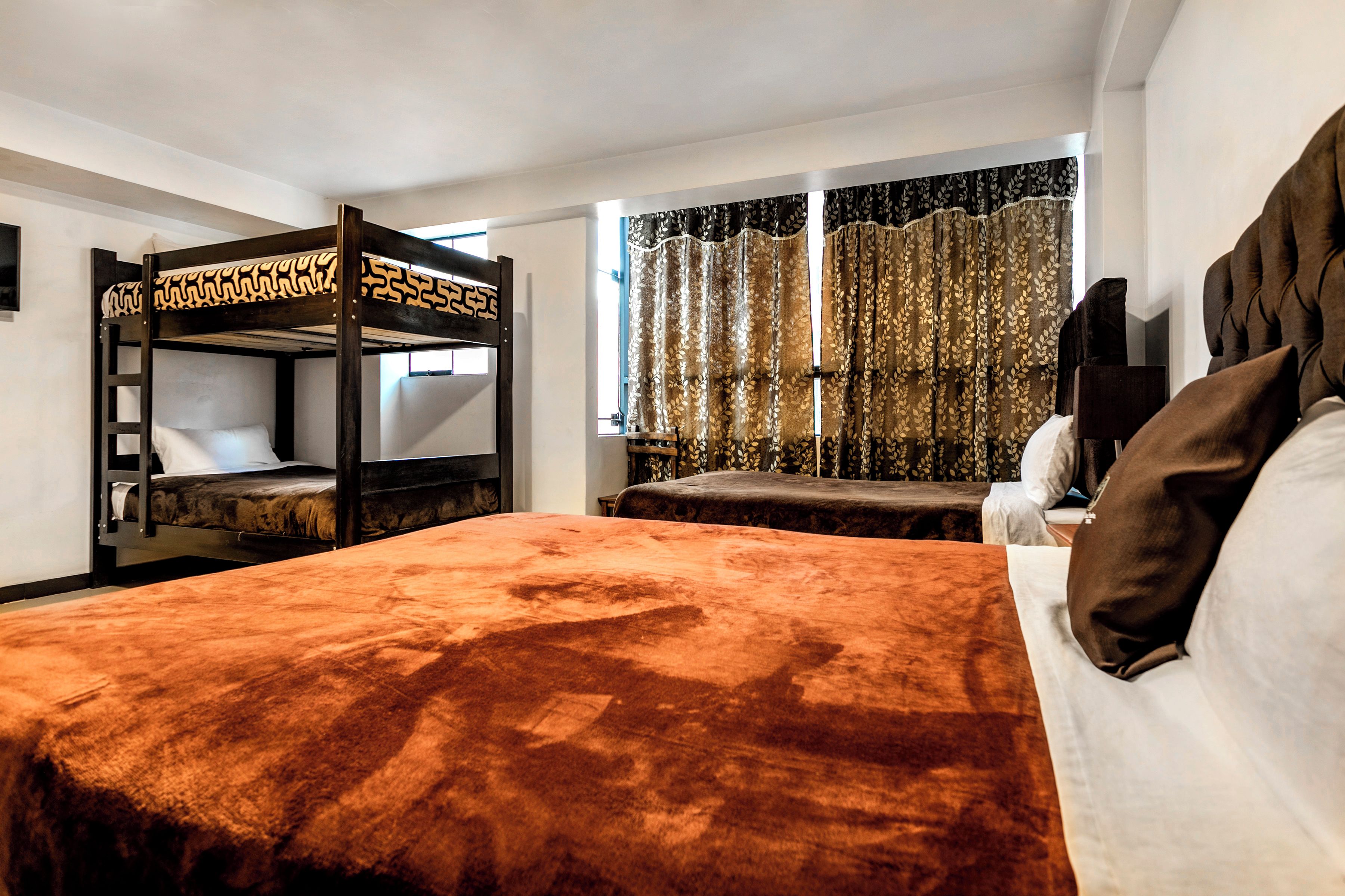 A bunk bed room with a brown headboard, a window with curtains, and a bed with a brown cover.