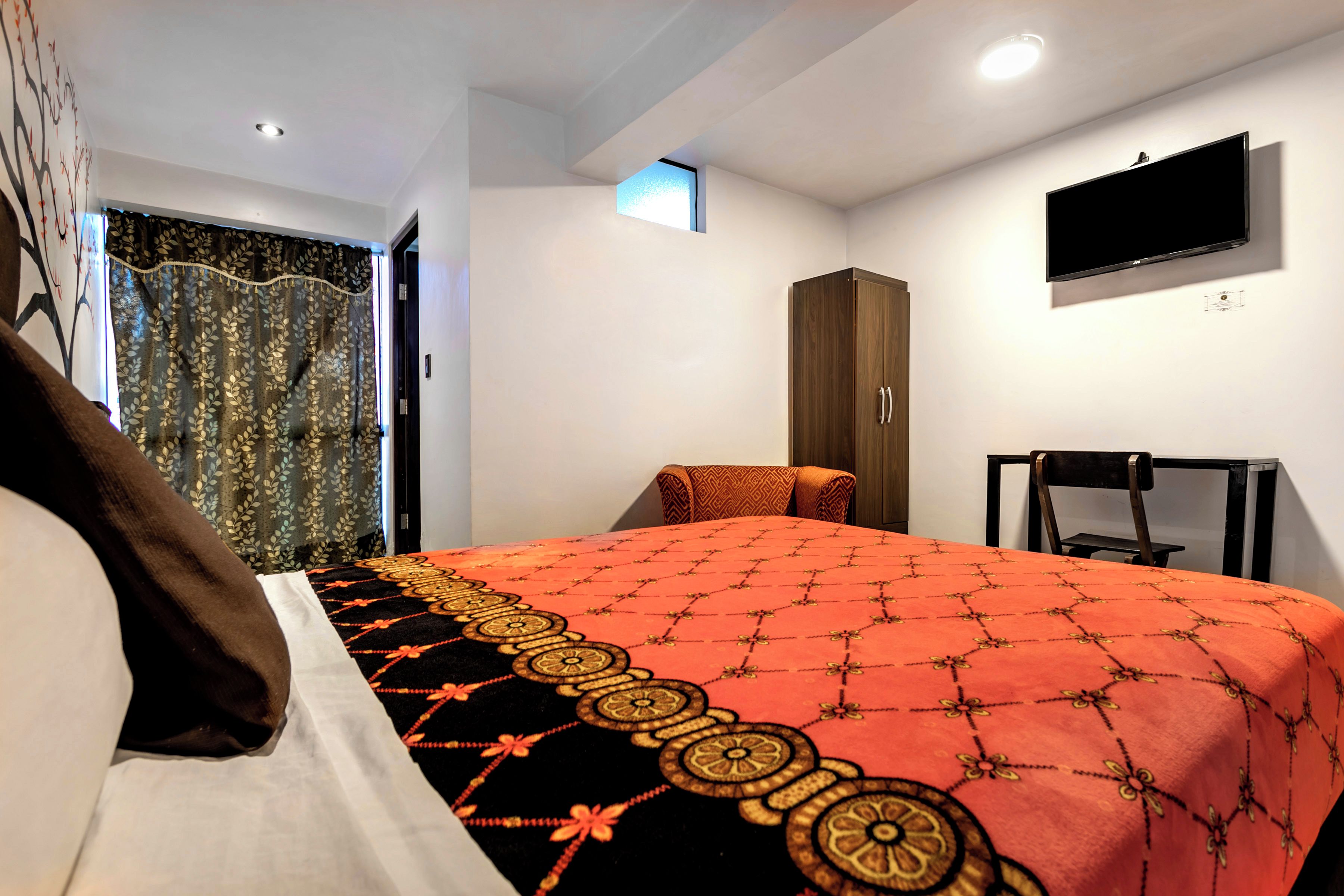 A hotel room with a bed, a wardrobe, a television, and a window with curtains.