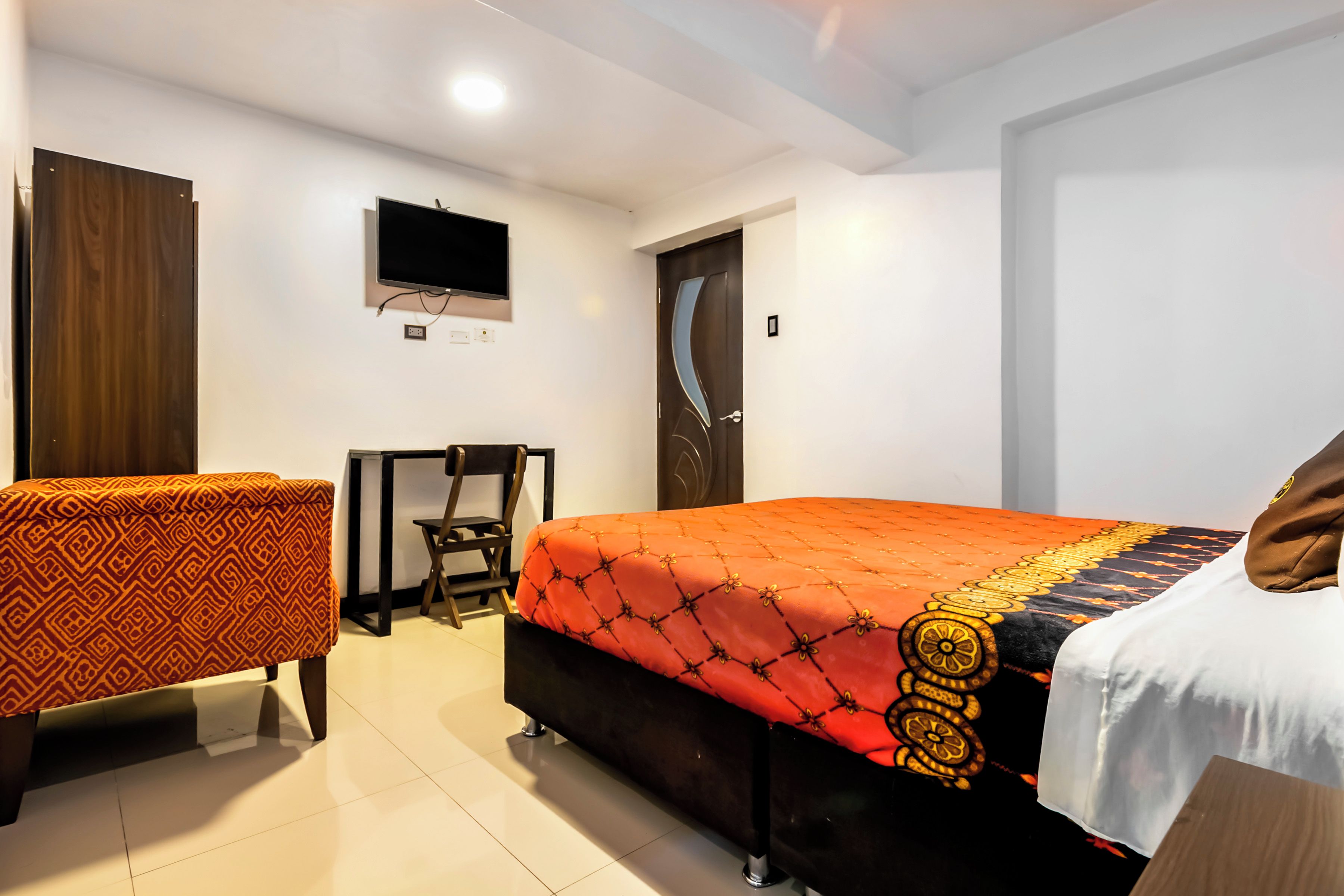 A hotel room with a bed, a desk, a chair, a television, and a door.