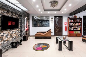 A modern lobby with a stone wall, a Netflix screen, a sofa, a coffee table, a bookshelf, and a fire extinguisher. - Hidden Garden (Cusco)