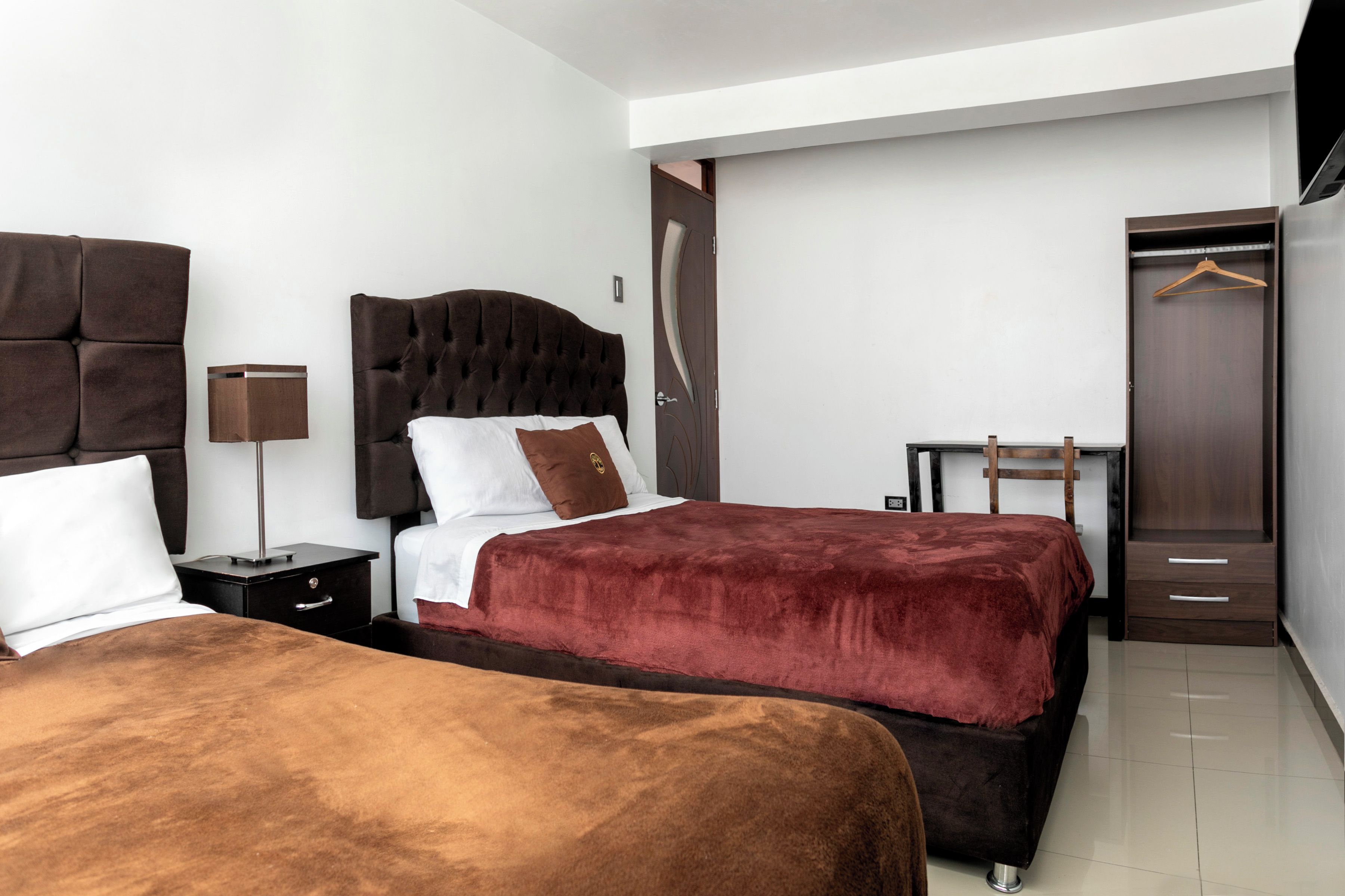 A hotel room with two beds, a wardrobe, a bedside table, and a hanging coat rack.