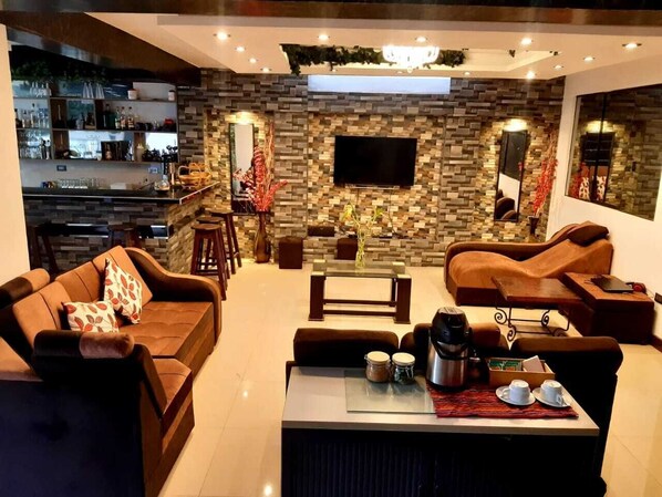 Uma sala de estar moderna com parede de pedra, TV de tela plana e mesa de centro com xícaras e cafeteira.