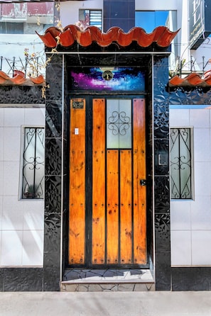 A hotel entrance with a wooden door, metal gates, and a decorative sign above the door. - Hidden Garden (Cusco)