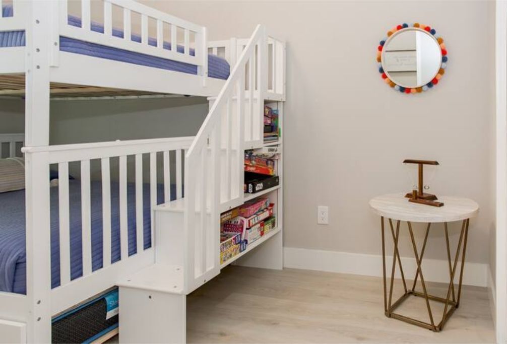A bunk bed with a bookshelf underneath, a round mirror on the wall, and a small round table with a lamp.