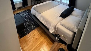 Quarto com cama, escrivaninha e cadeira. Possui duas janelas com cortinas.