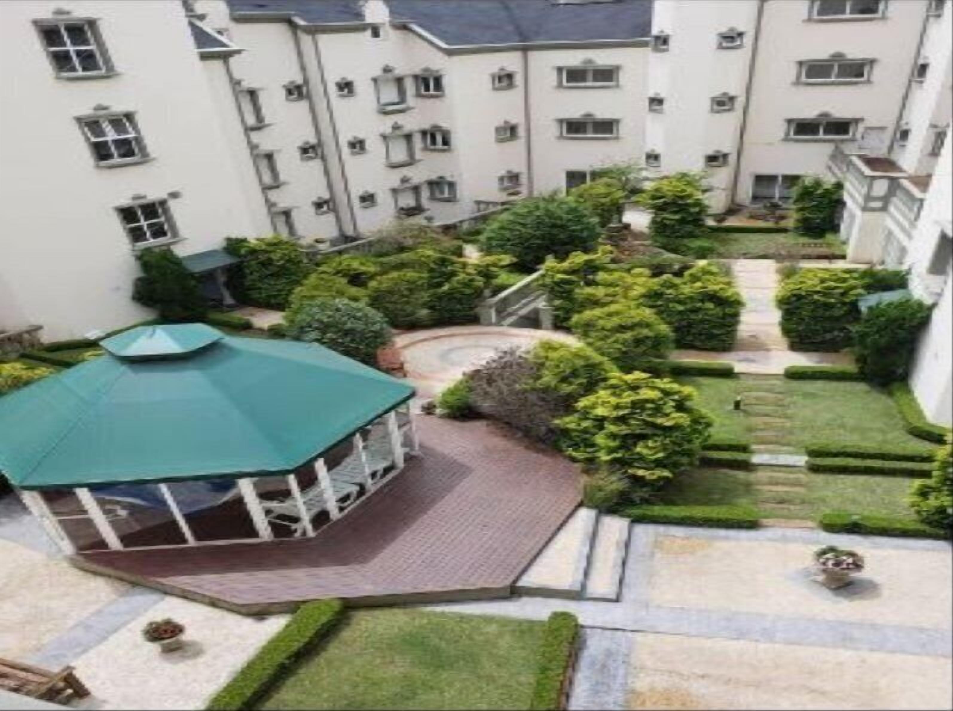Um pátio com um gazebo, gramados bem cuidados e um edifício com várias janelas e sacadas.