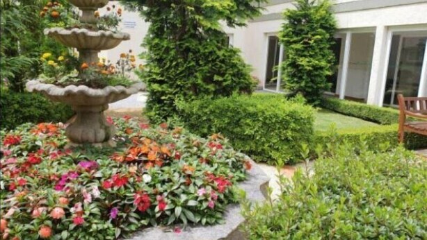 Ein Garten mit einer mehrstufigen Springfontäne, umgeben von bunten Blumen und gepflegten Hecken.