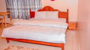 A bed with a wooden frame and white bedding in a room with a tiled floor. - mountain view apartment (Kigali)
