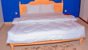 A double bed with a wooden headboard and white bedding in a room with blue walls and a patterned rug. - mountain view apartment (Kigali)