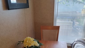 Una mesa de madera para comer con un ramo de flores amarillas, una silla y una ventana con persianas.