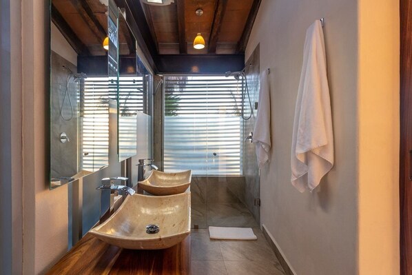 A modern bathroom with a wooden vanity, two sinks, a large mirror, and a shower area.
