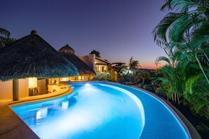 A swimming pool with a curved edge, surrounded by palm trees and thatched-roof structures.