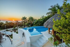 A swimming pool with a view of the sunset, surrounded by palm trees and a thatched-roof structure. - Villa Bellavista 2 (Santa María Huatulco)