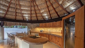 Una cocina con una isla central, armarios de madera, un refrigerador de acero inoxidable y un techo de paja.