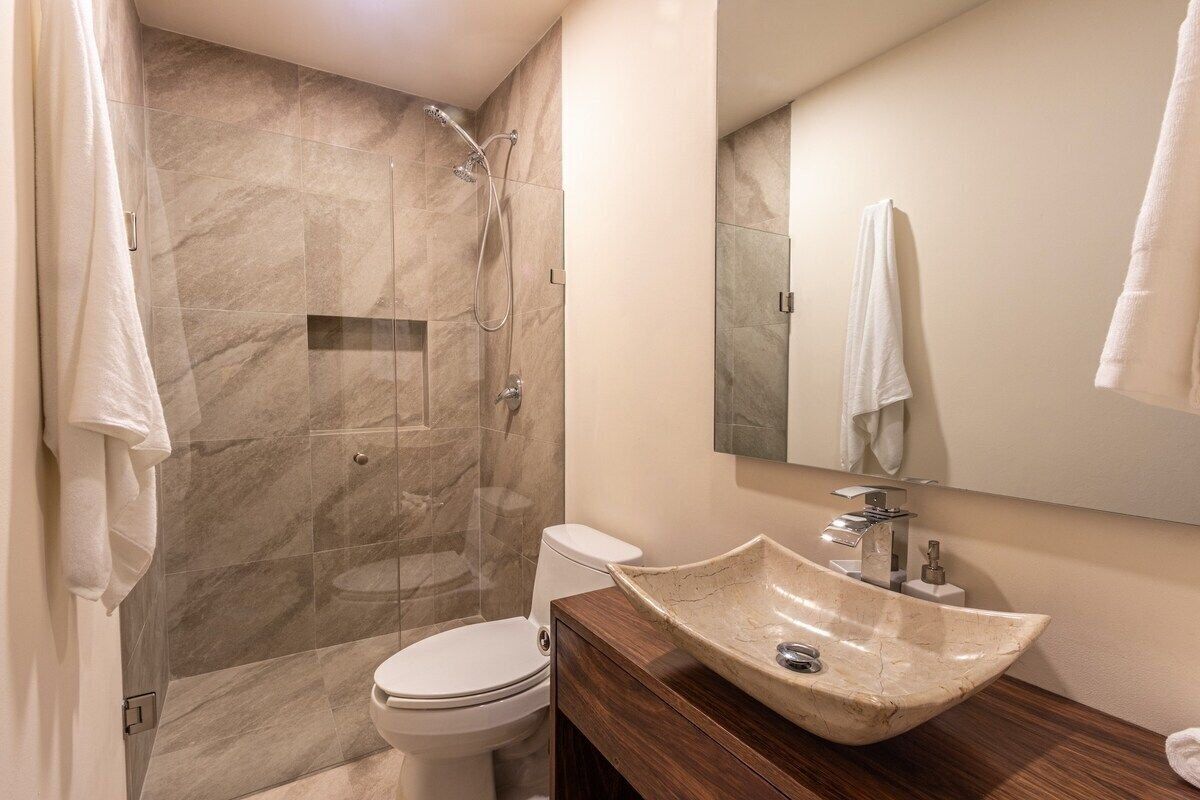 A bathroom with a marble shower, a white toilet, a wooden vanity with a sink, and a mirror.