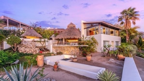 Un resort con un edificio moderno, una estructura de techo de paja y un jardín bien cuidado con diversas plantas.
