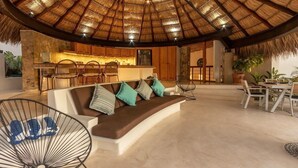 Un espacio habitable de concepto abierto con techo de paja, una cocina y arreglos de asientos.