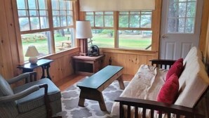 Un acogedor interior de cabaña con paredes de madera, un banco, una silla y un sofá con cojines rojos.