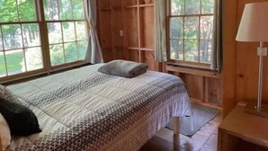 Habitación de cabaña de madera con cama, ventanas amplias y una lámpara.