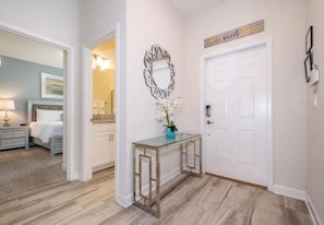 A hallway with a white door, a decorative mirror, and a small table with a vase of flowers.