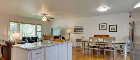 A modern kitchen with white cabinetry, a granite countertop, and a dining area with a wooden table and chairs.