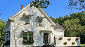 A two-story house with a gabled roof, a front porch, and a small front yard. - Renovated Turn Of The Century Three Bedroom Farmhouse (Rockport)