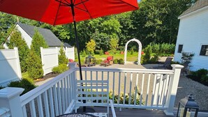 A wooden deck with a table and chairs, a red umbrella, and a white fence. - Renovated Turn Of The Century Three Bedroom Farmhouse (Rockport)