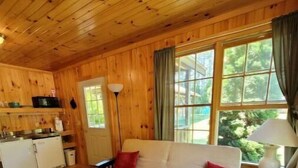 A cozy cabin interior with a wooden ceiling, a sofa with red cushions, a dining table, and a window with curtains. - Private Cabin with access to Rust Pond Ferris (Wolfeboro)