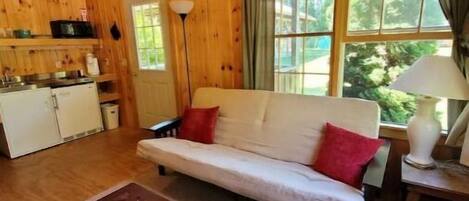 Interior acogedor de una cabaña con techo de madera, un sofá con cojines rojos, una mesa de comedor y una ventana con cortinas.