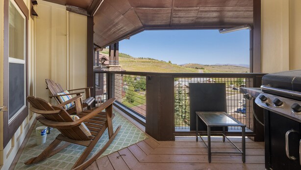 A balcony with a view of a hilly landscape, a grill, and a rocking chair. - Ski-In/Ski-Out Top Floor with Views and Amenities- Heated Parking Garage (Granby)