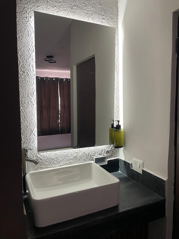A bathroom with a white sink, a mirror with a textured frame, and a shower curtain. - Yolotl Sleep Experience (Piedras Negras)