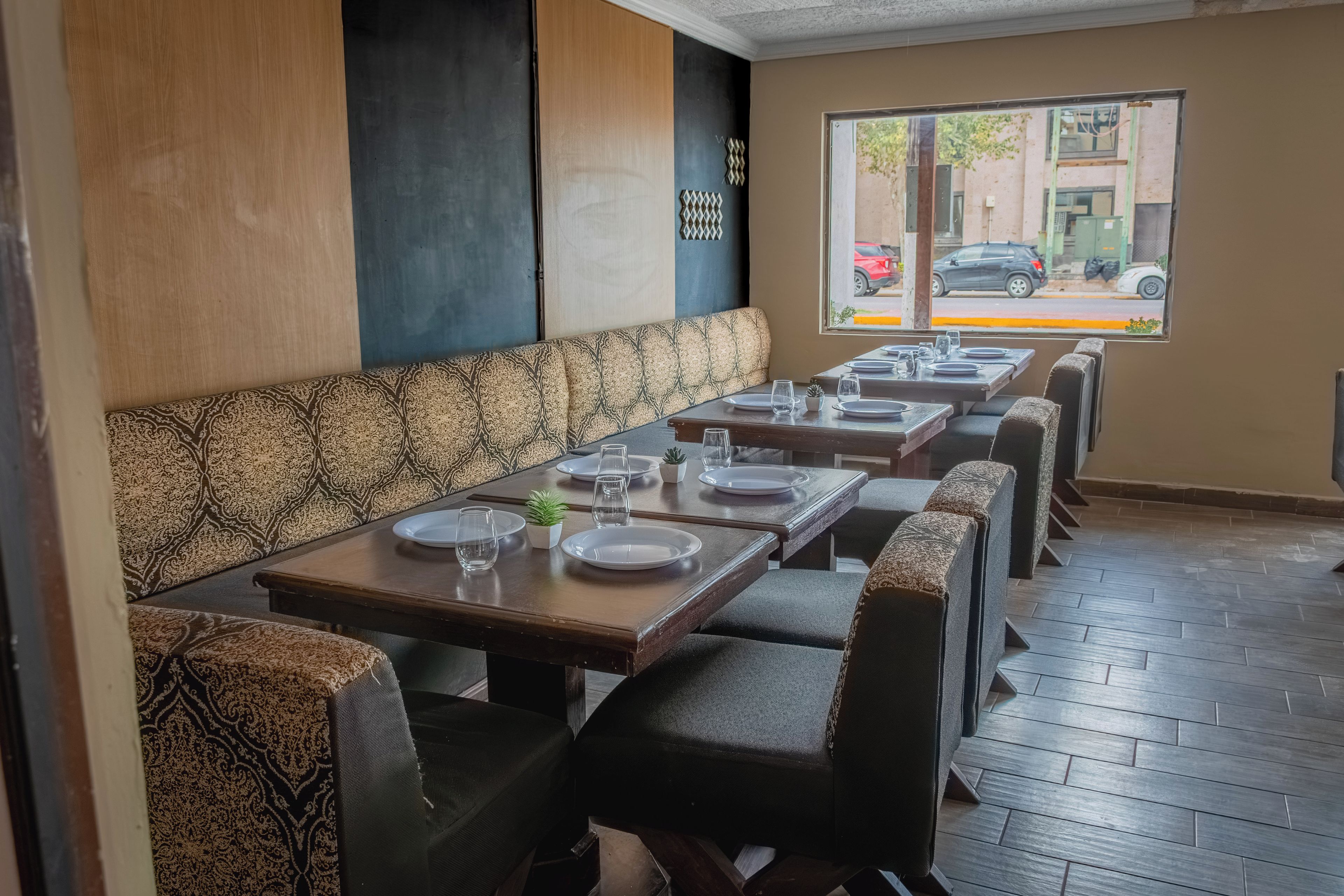 L’intérieur d’un restaurant avec de longues banquettes, des tables dressées avec des assiettes et des verres, et une fenêtre donnant sur la rue.