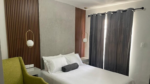 A neatly arranged hotel room with a single bed, a green armchair, and a bedside table with a lamp. - Yolotl Sleep Experience (Piedras Negras)