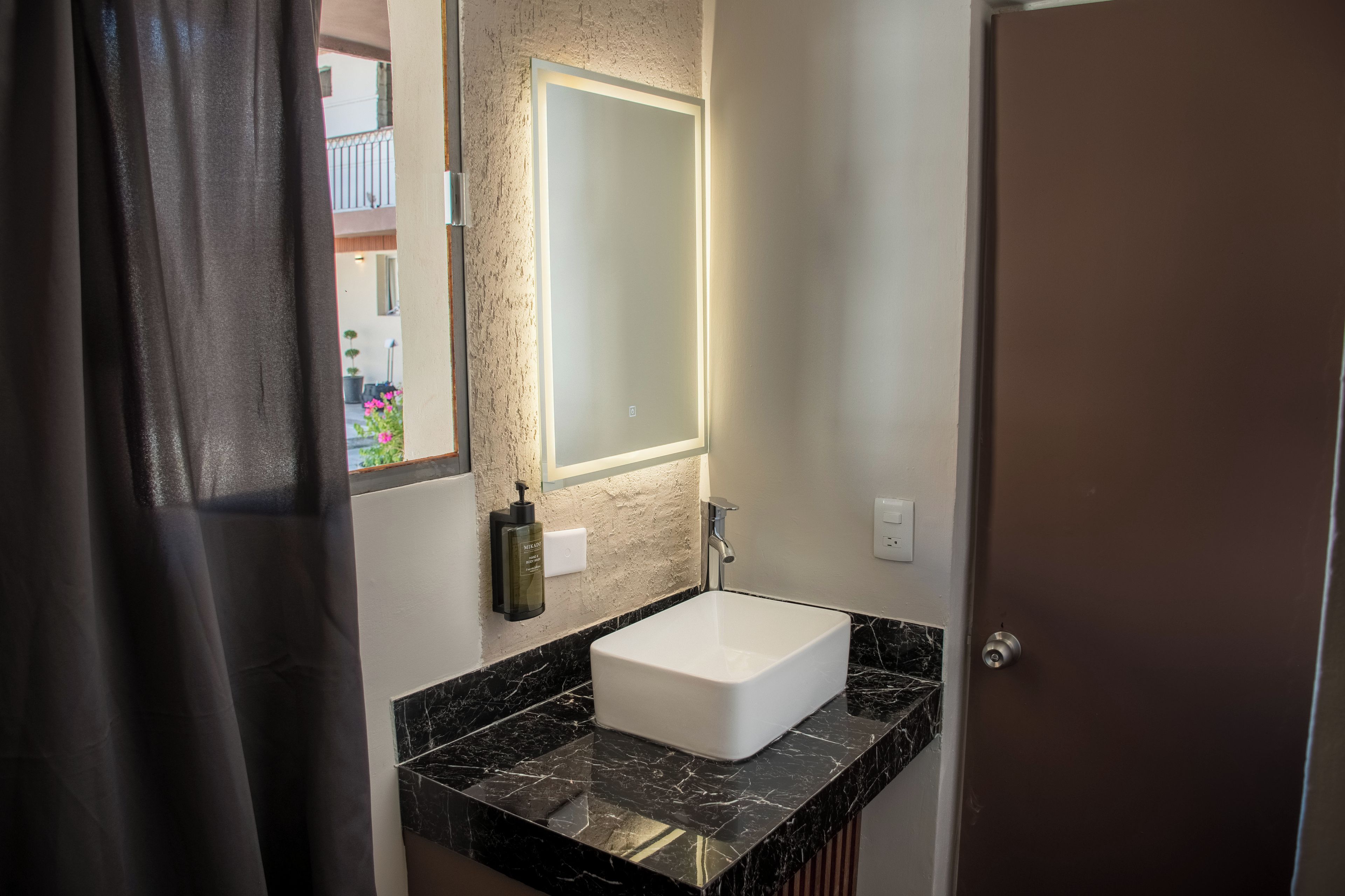Une salle de bain avec un lavabo blanc, un plan de toilette en marbre noir et un miroir surmonté d’une lampe.