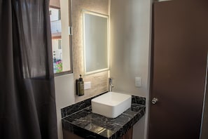 A bathroom with a white sink, black marble countertop, and a mirror with a light above it. - Yolotl Sleep Experience (Piedras Negras)