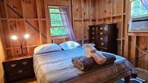Une chambre dans une cabane en bois, comprenant un lit, une table de chevet, une commode, un ventilateur de plafond et une fenêtre avec des rideaux.
