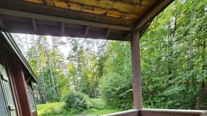 Une véranda avec deux chaises en plastique vertes, une terrasse en bois et une vue sur une zone boisée.