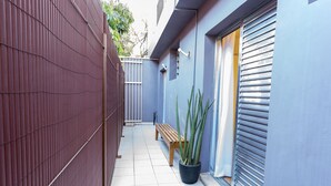 A narrow alleyway with a wooden bench, a potted plant, and a metal fence. - Apartamento 2 Quartos - Praça Pôr do Sol (São Paulo)