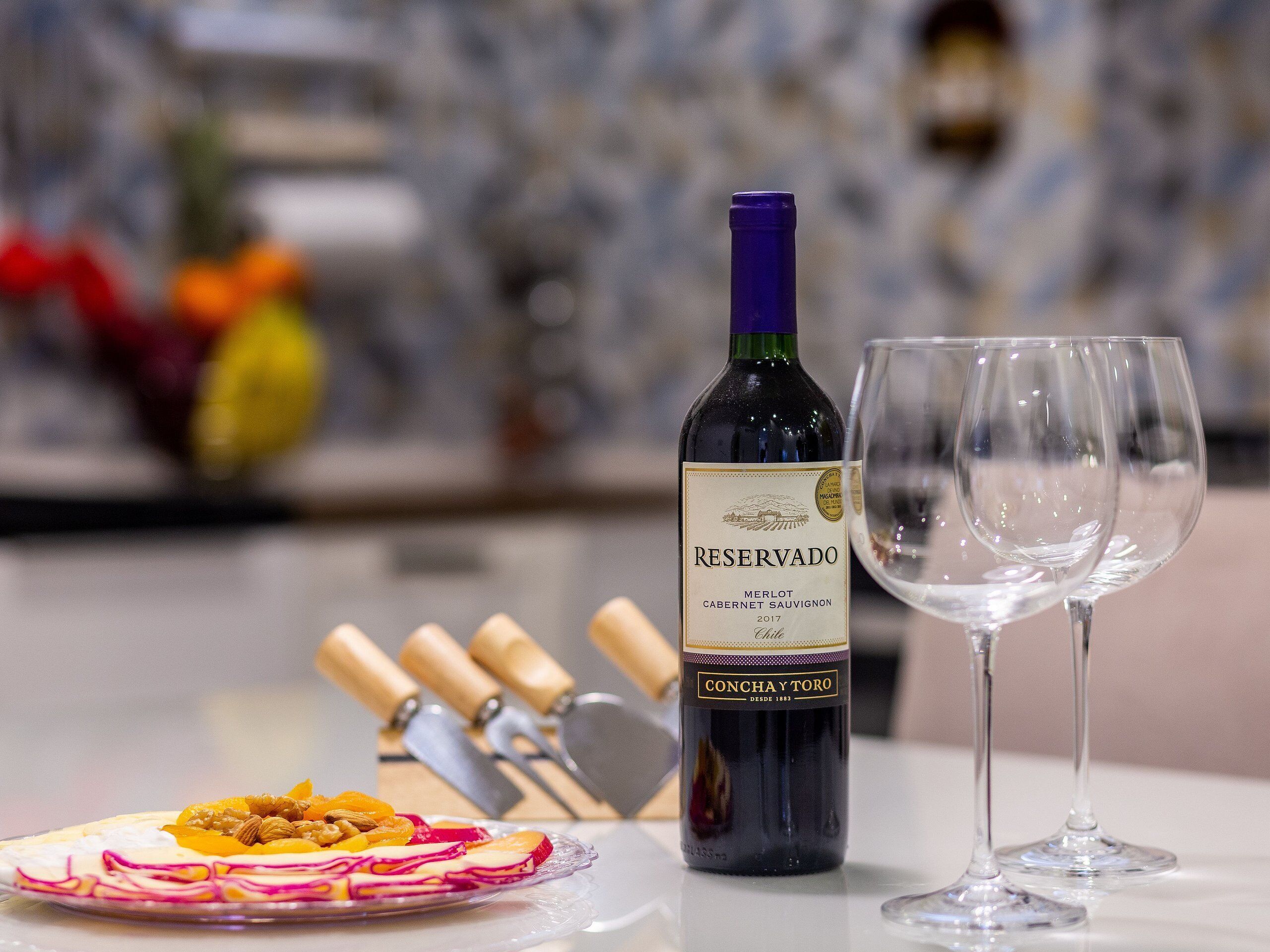 Une bouteille de vin rouge Merlot, un verre et une assiette de nourriture sur une table.