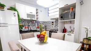 A modern kitchen with white cabinetry, a dining table with chairs, and a fruit bowl on the table. - Apartamento 2 Quartos - Praça Pôr do Sol (São Paulo)