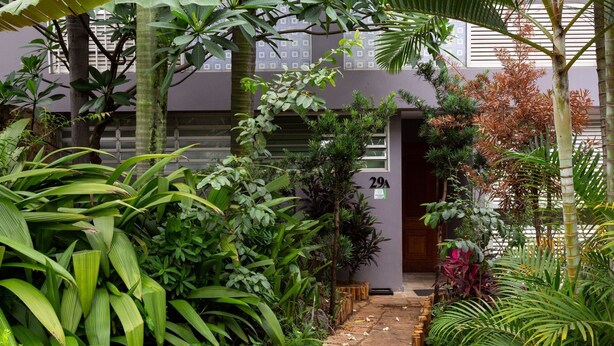 A lush garden with a stone pathway leading to a building entrance marked with the number 29A. - Apartamento 2 Quartos - Praça Pôr do Sol (São Paulo)